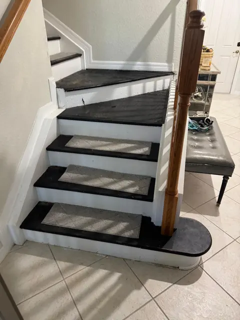 Escalera con escalones pintados de negro y alfombrillas, antes